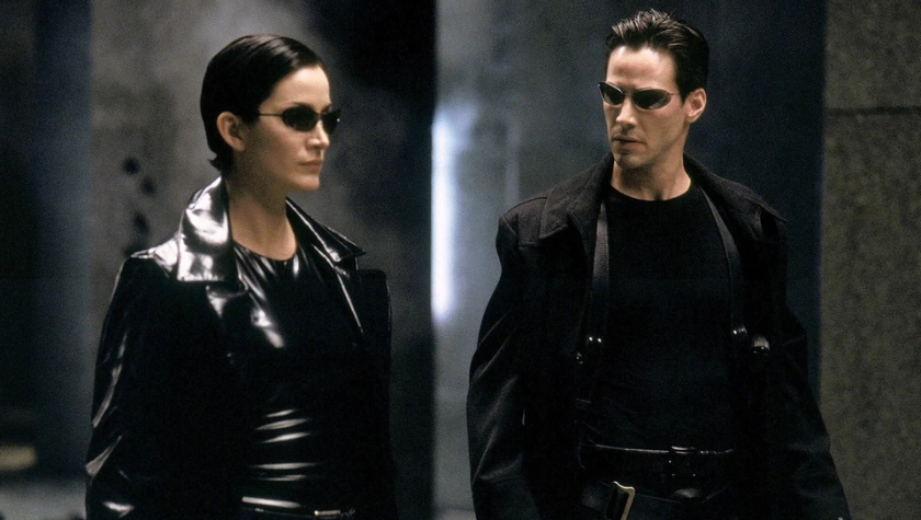 Neo and Trinity walk side by side in matching black leather in a still from The Matrix (1999)
