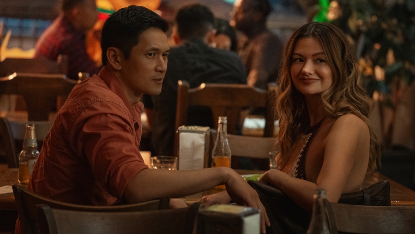 A man and woman sitting close together at a restaurant bar, glancing at each other