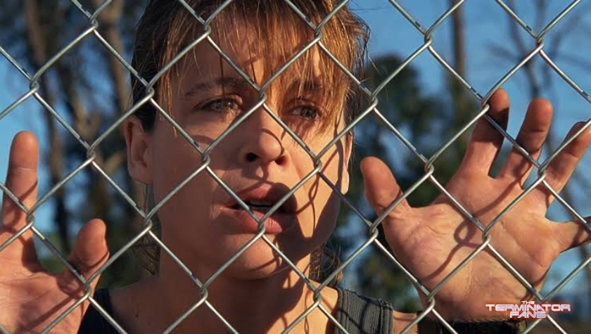 Sarah Connor grips a chain-link fence, a recurring image from her nuclear nightmare in The Terminator