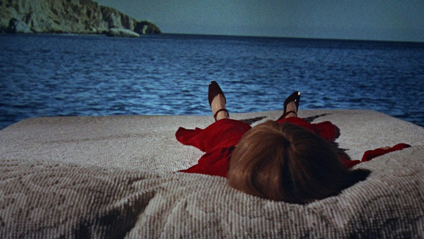 A woman in red lies on a surface by the sea in a dreamlike scene from Rosemary's Baby