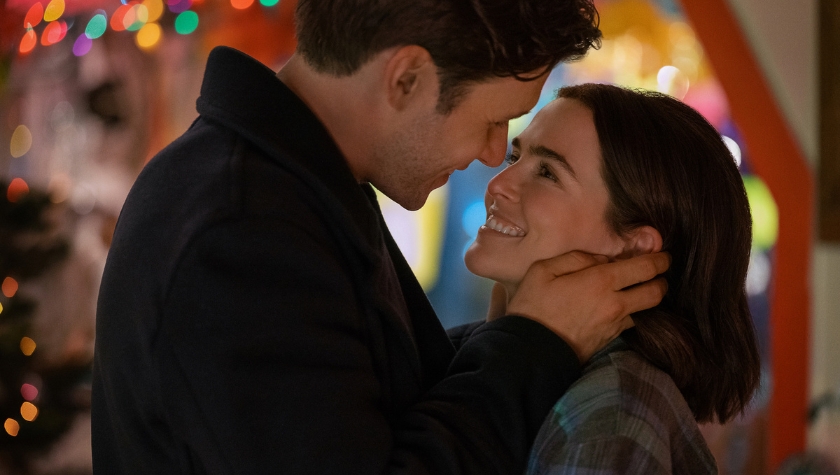 Jill and Wes in an intimate moment, about to kiss, surrounded by colorful bokeh holiday lights