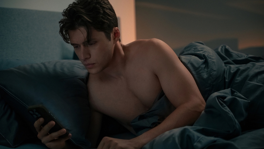 Nick Robinson as Wes lying in bed looking at his phone